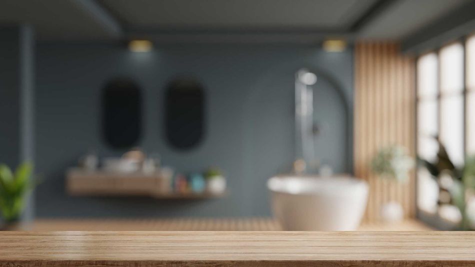 A blurred bathroom interior featuring a wooden tabletop in the foreground and a freestanding tub against a dark wall.