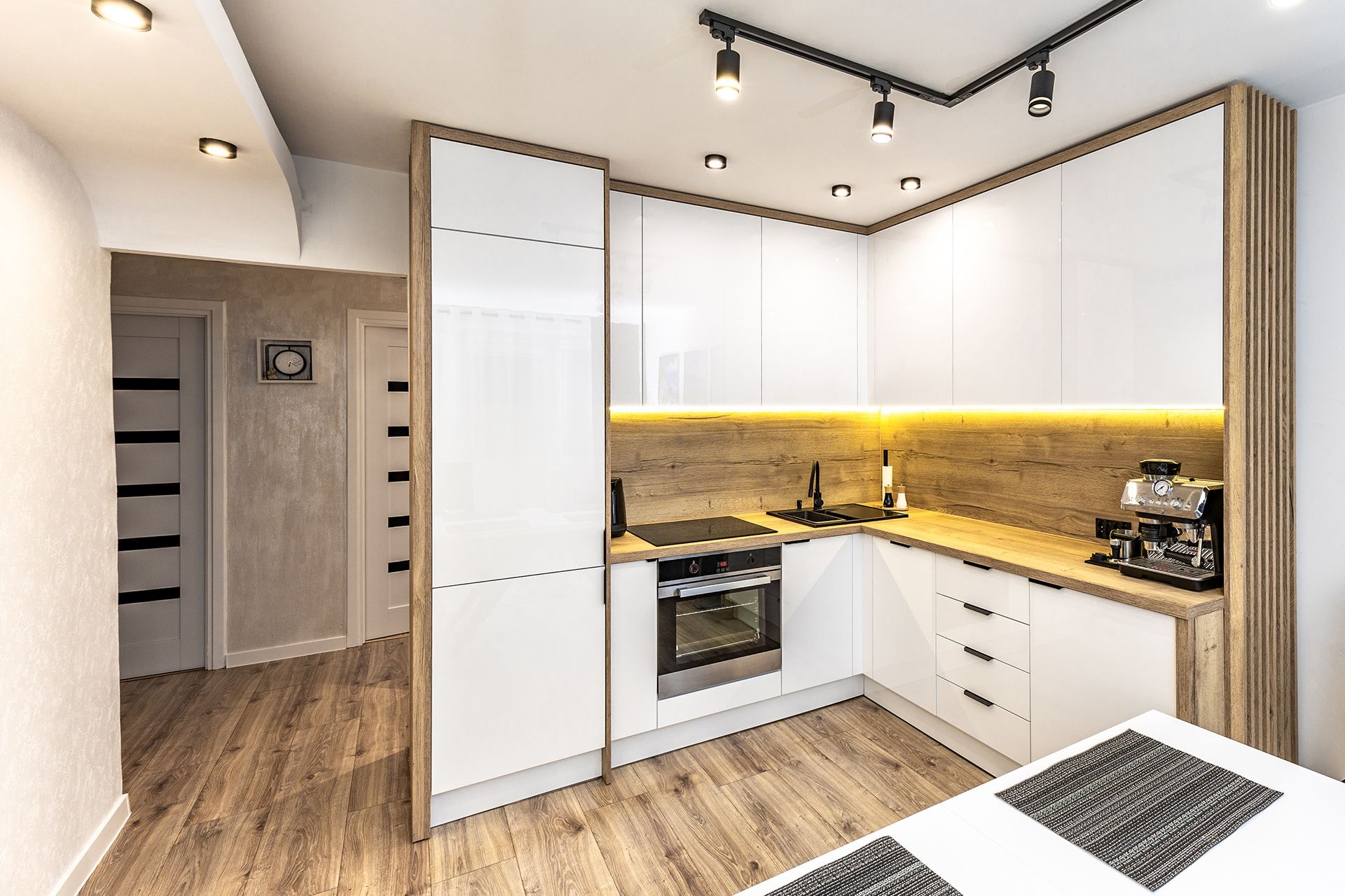 Modern white kitchen with wood flooring, black track lights, and warm under-cabinet lighting