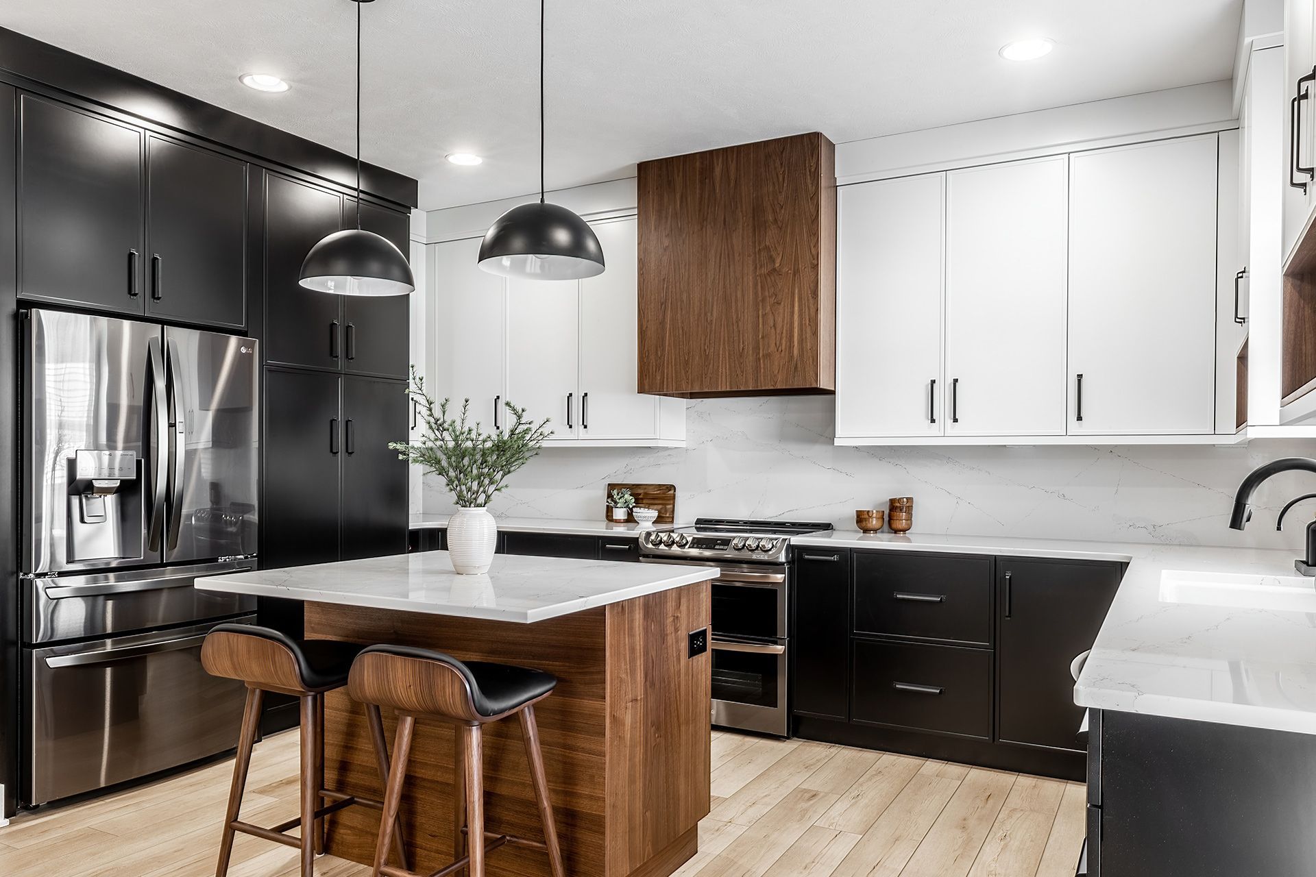 Modern kitchen with black and white cabinets, a wood-toned island and hood, stainless steel appliances, and wood floors.