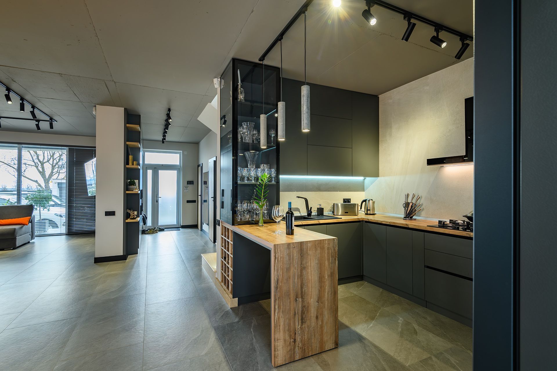 A modern kitchen with dark cabinets, a wood-grain breakfast bar, and track lighting in an open-concept interior.