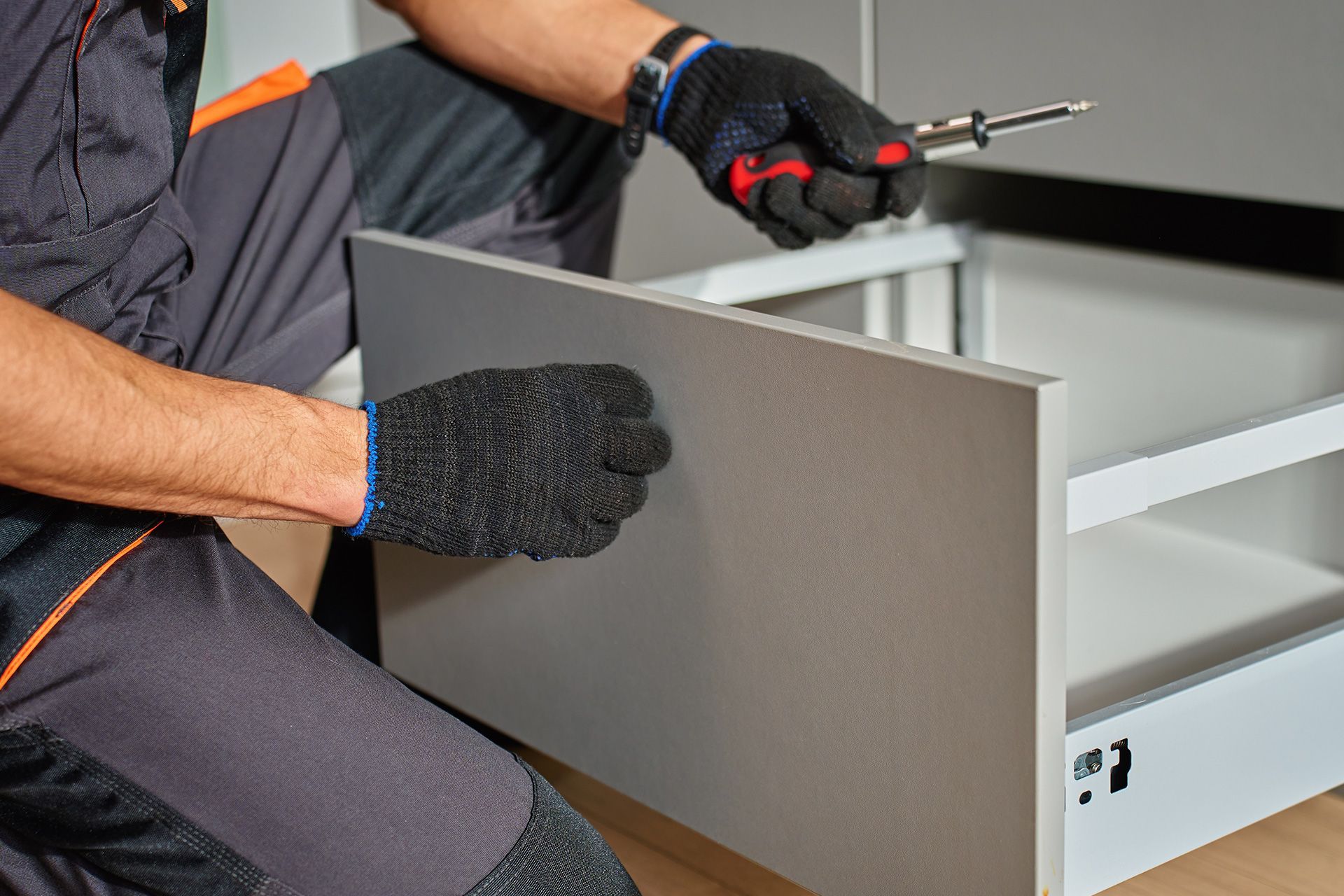 Person wearing gloves assembling a gray drawer or cabinet in a workshop
