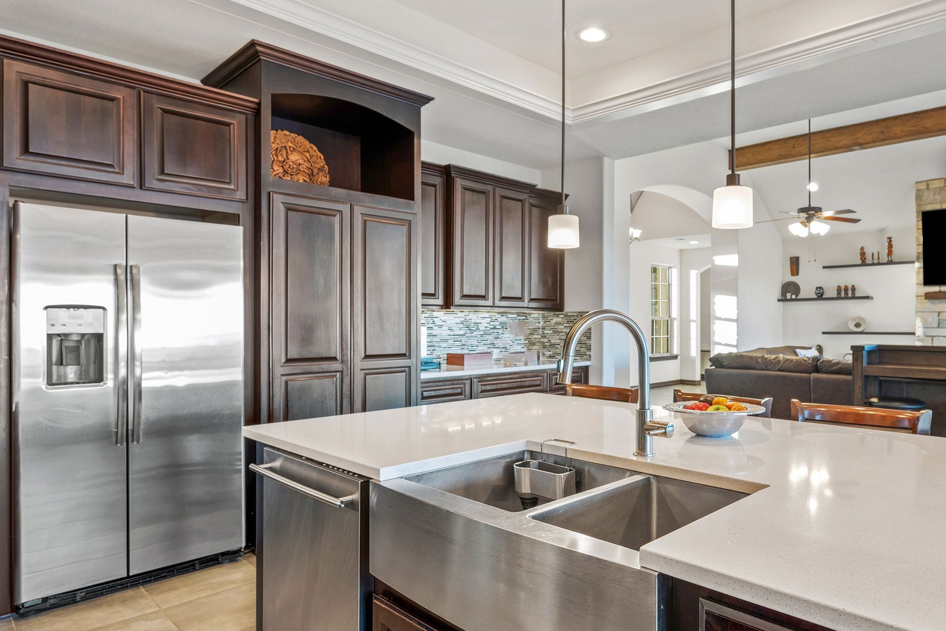 A modern kitchen with dark wood cabinets, stainless steel appliances, a white quartz island, and pendant lighting.