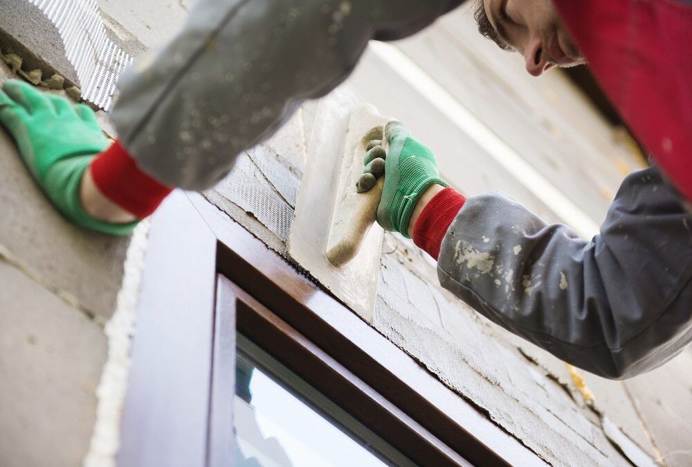 A Man is Plastering a Window Frame With a Trowel — Central Coast Property Maintenance Services In Umina Beach, NSW