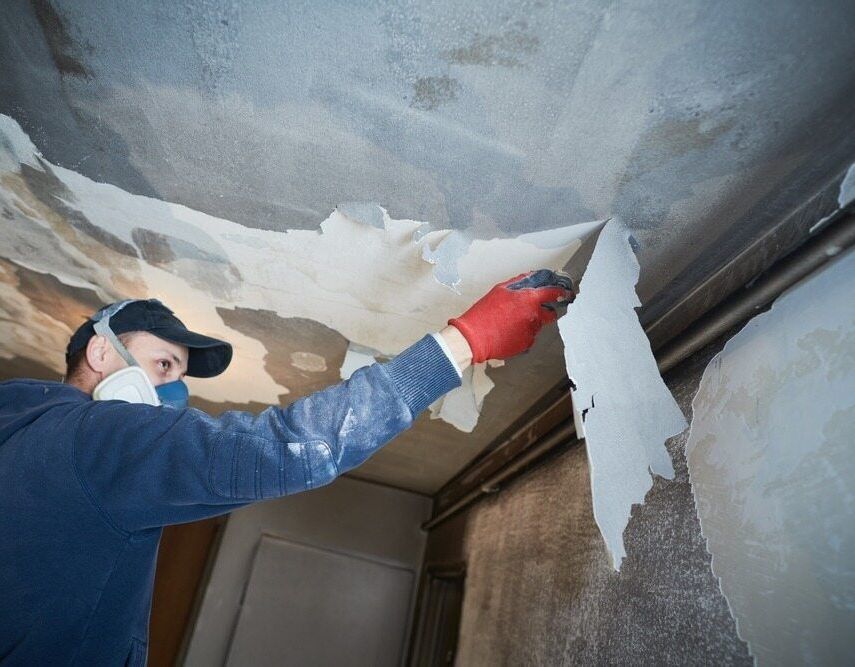 A Man Wearing a Mask and Gloves is Peeling Paint From the Ceiling — Central Coast Property Maintenance Services In Gosford, NSW