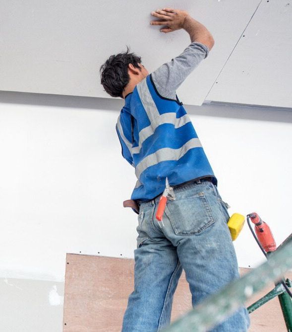 A Man in a Blue Vest is Working on a Ceiling — Central Coast Property Maintenance Services In Ettalong, NSW