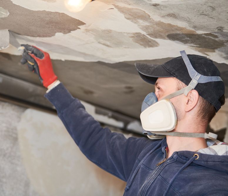 A Man Wearing a Mask and Gloves is Plastering a Ceiling — Central Coast Property Maintenance Services In Kincumber, NSW