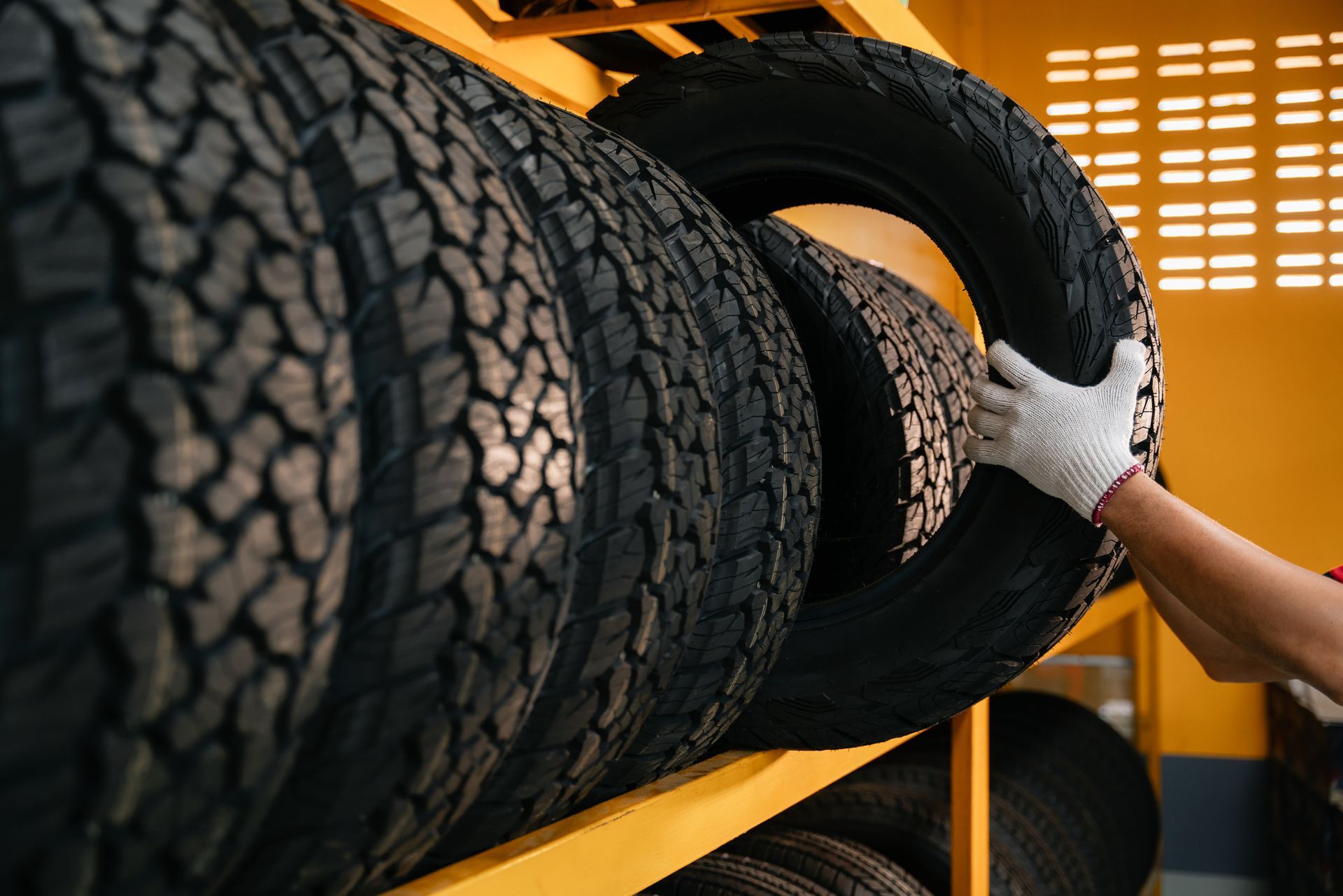 Hand of a tire changer lifting a car tyre out of a warehouse.