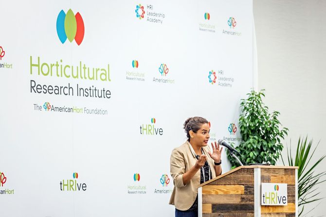a woman stands at a podium in front of a wall that says horticultural research institute