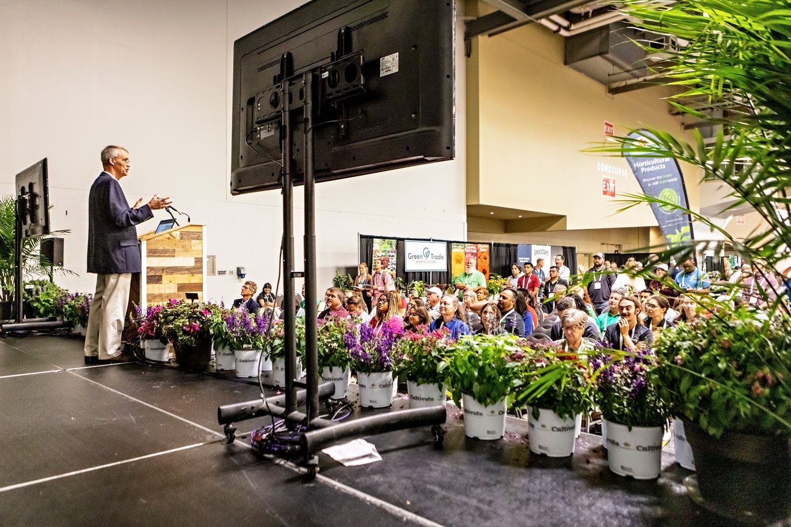 a man stands at a podium giving a presentation in front of a sign that says grow fresh