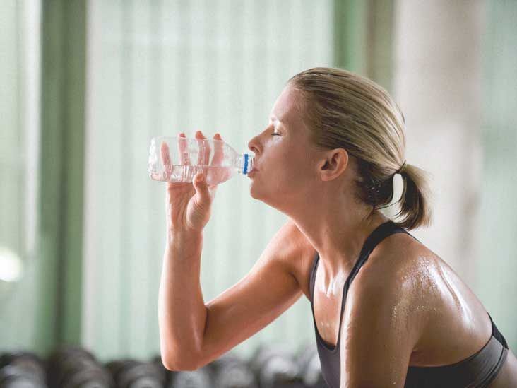 A woman is drinking water from a bottle in a gym.