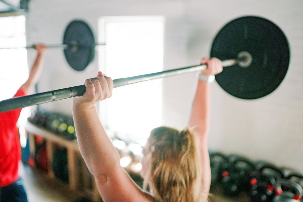 A woman is lifting a barbell over her head in a gym.