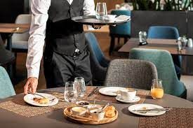 A waiter is carrying a tray of food to a table in a restaurant.