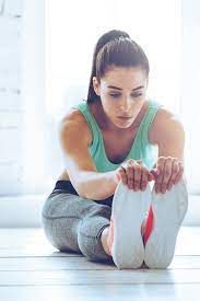 A woman is sitting on the floor stretching her legs.