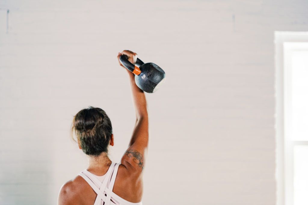 A woman is lifting a kettlebell over her head in a gym.