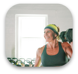 A woman is smiling while lifting a dumbbell in a gym