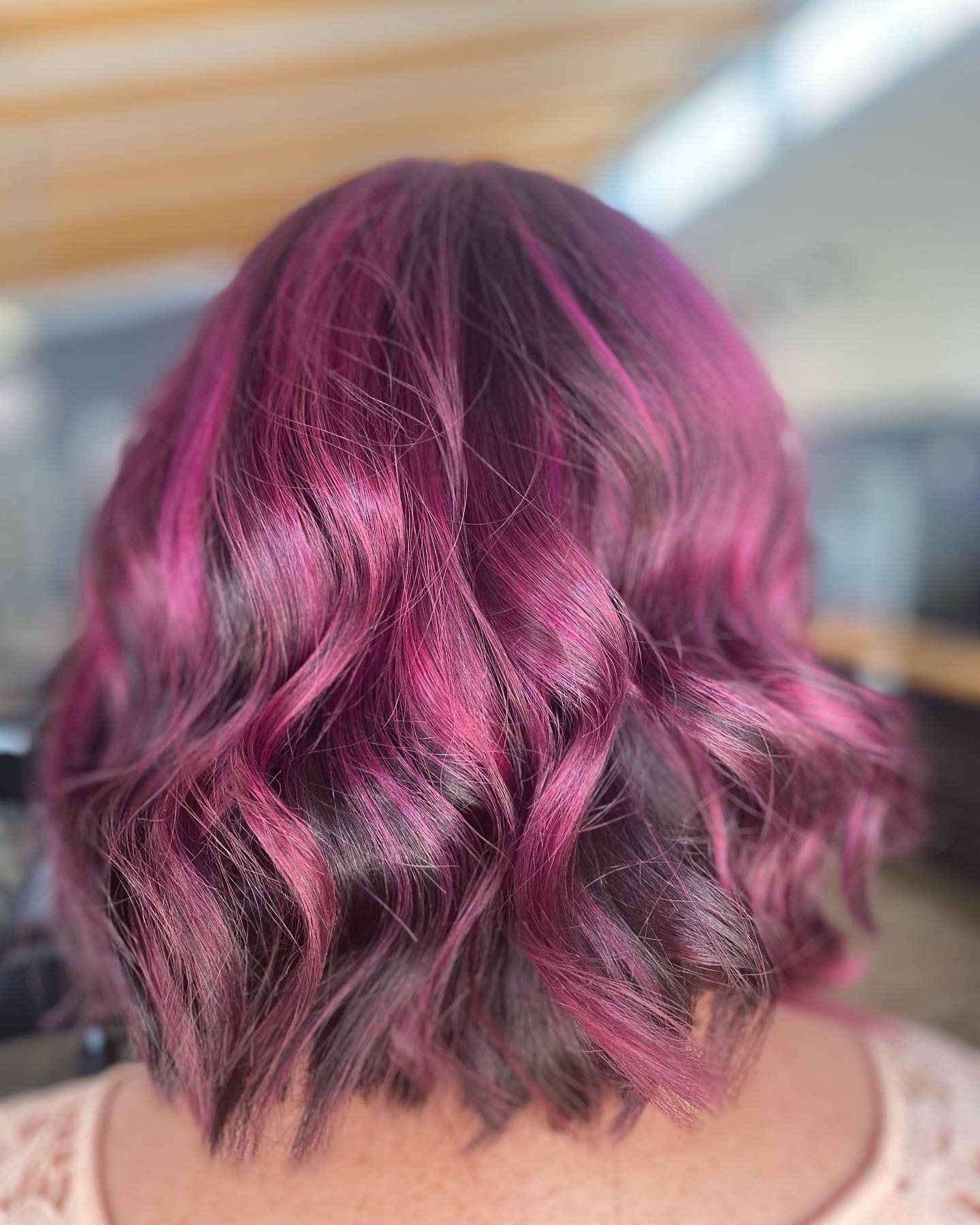 Woman with short, wavy, magenta and dark purple hair.
