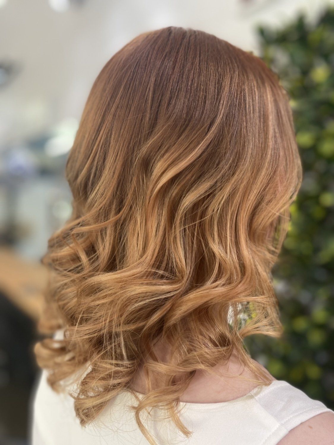 Woman with wavy, auburn hair, styled in layers. The hair is shoulder-length with lighter highlights.