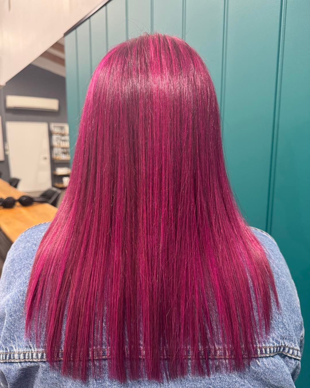 Woman with long, vibrant pink hair, seated in a salon.