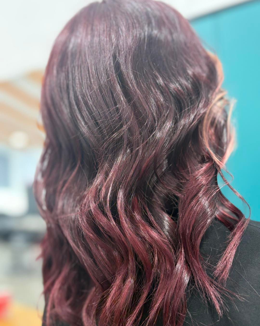 Woman with wavy, dark red hair, likely styled in a salon, against a blue wall background.
