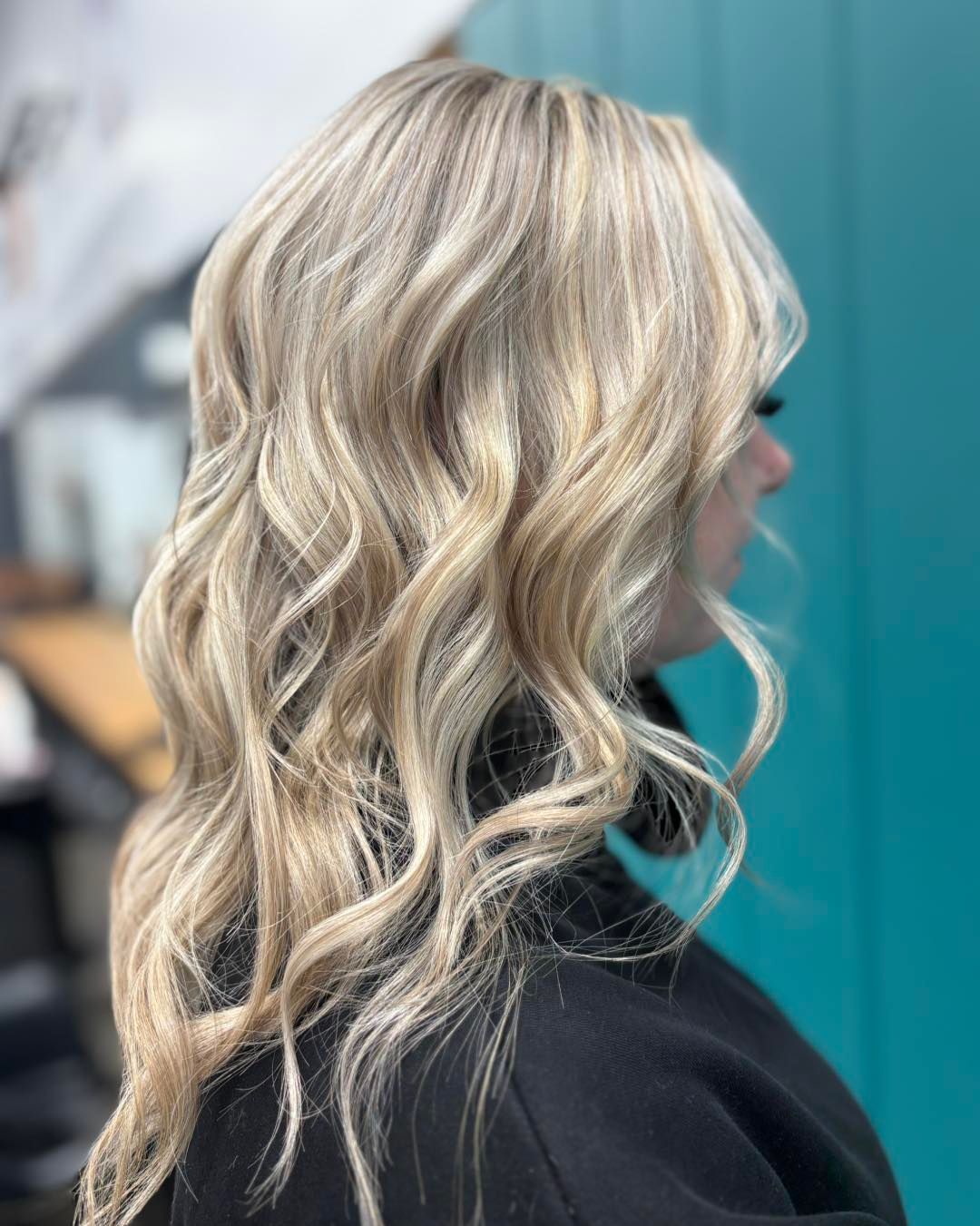 Woman with wavy blonde hair, styled with highlights, against a teal backdrop.