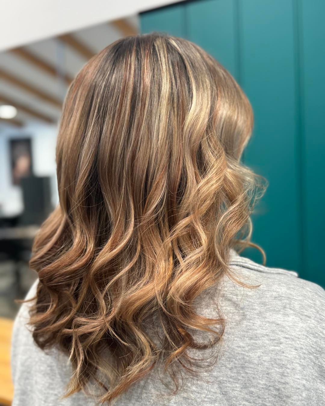 Woman with brown hair, wavy with blonde highlights, in a salon setting.