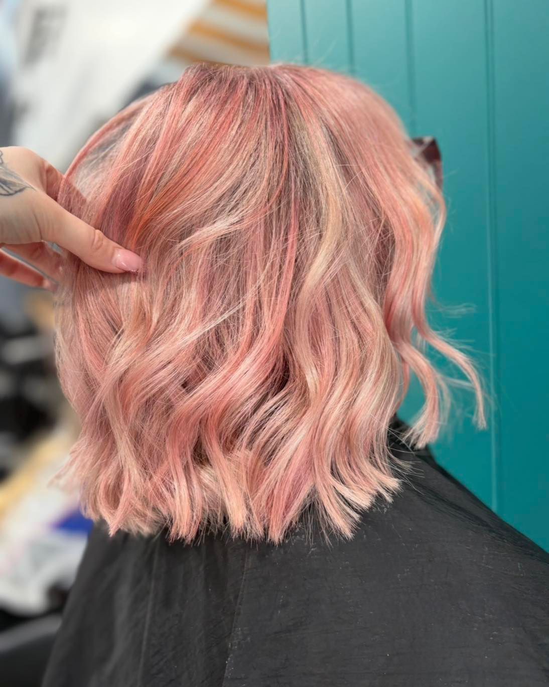Pink wavy bob hairstyle, hand touching hair.