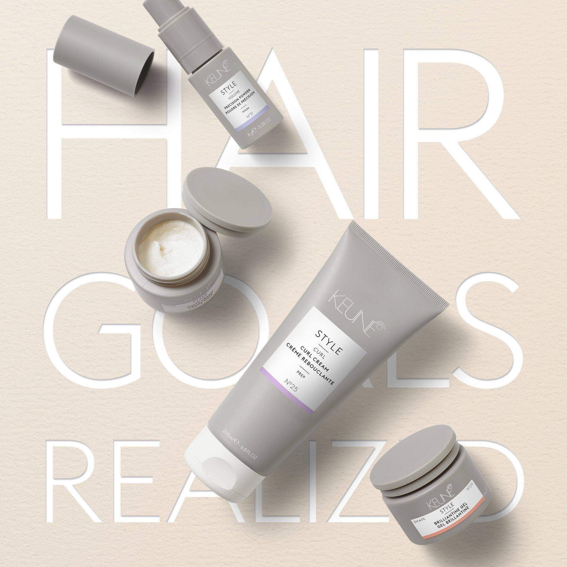 Hair products styled on a tan background. Gray bottles and tubes, with text “HAIR GOALS REALIZED”.
