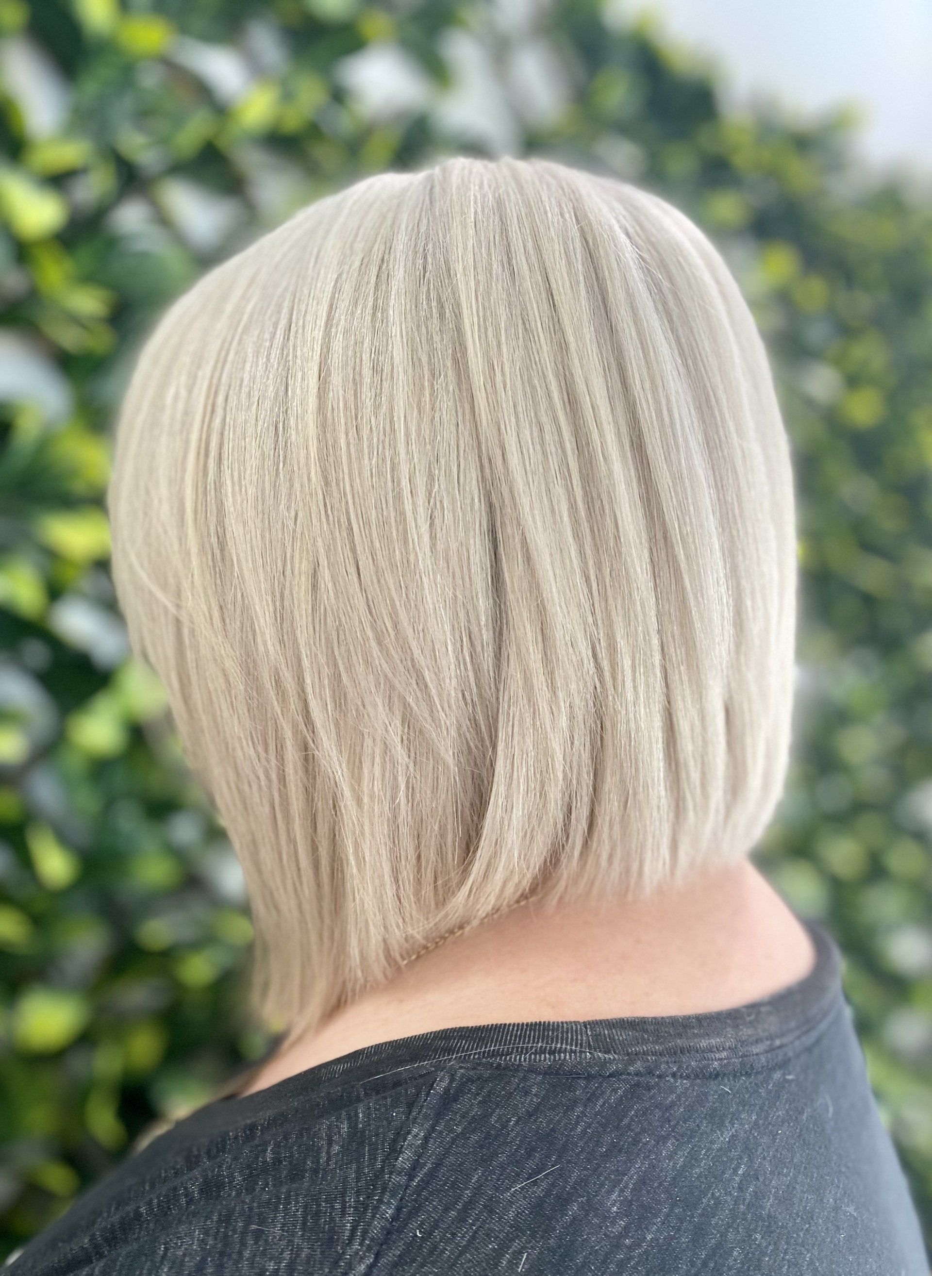 Blonde bob haircut with crimped texture, angled from the back against a green backdrop.