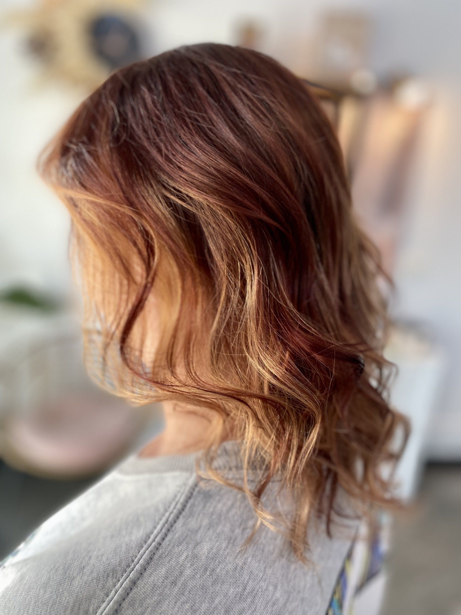 Woman with wavy, reddish-brown hair, sunlight highlighting the strands.