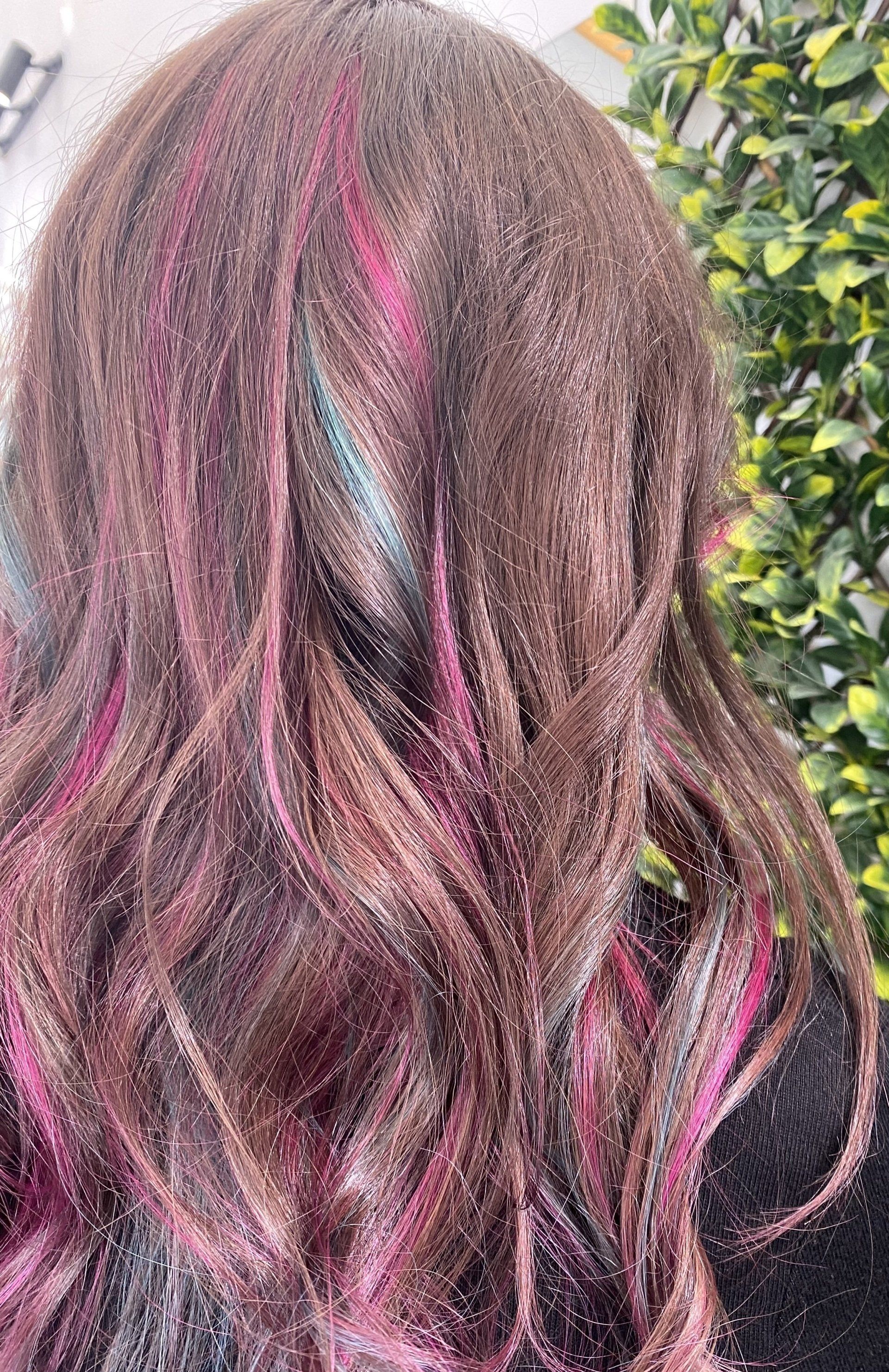 Woman's brown hair with pink and blue streaks, styled with waves.