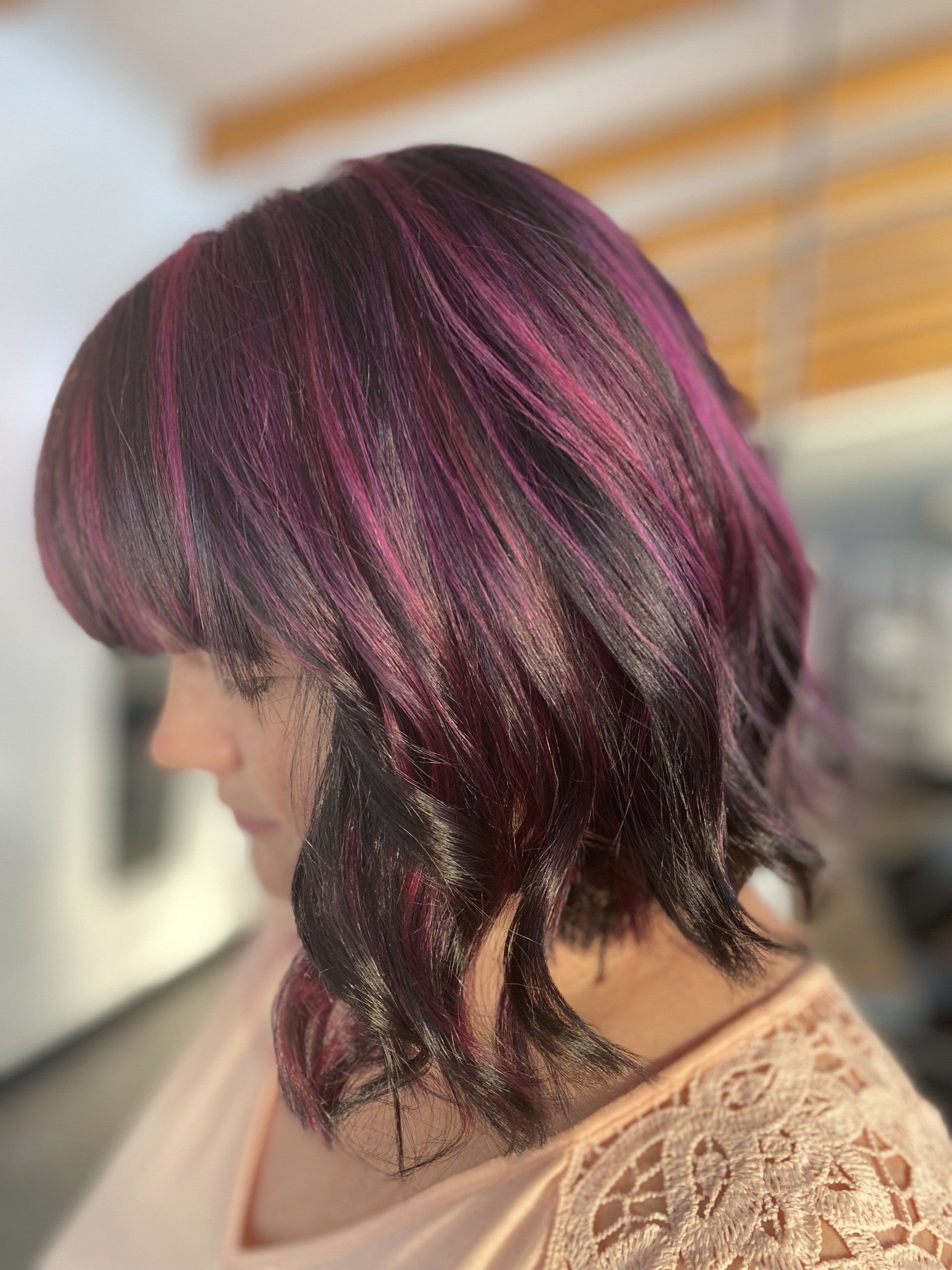 Woman with shoulder-length hair, dark roots blending into a pink-purple, with fringe bangs.
