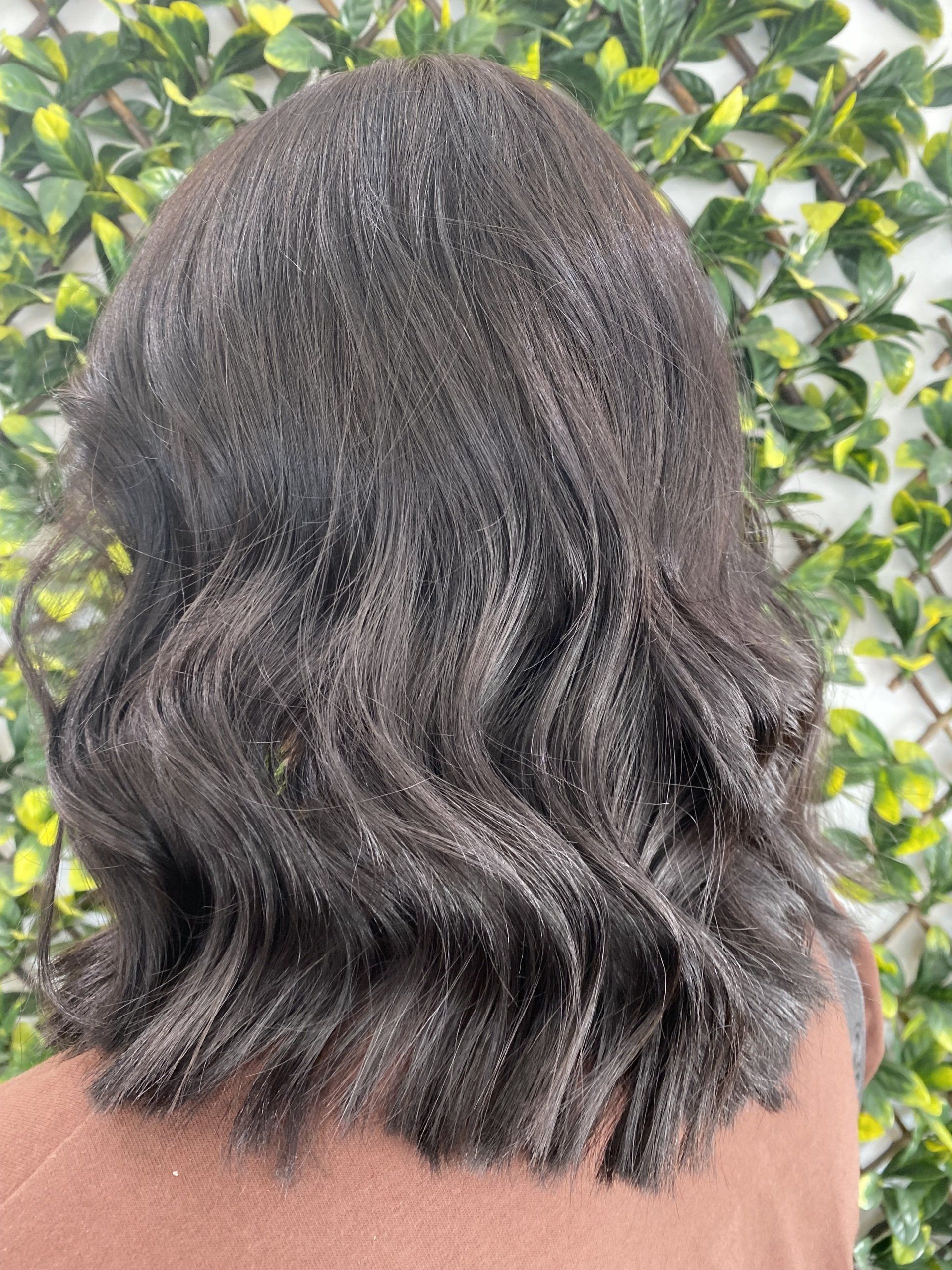 Woman with dark, wavy hair against a backdrop of green leaves.