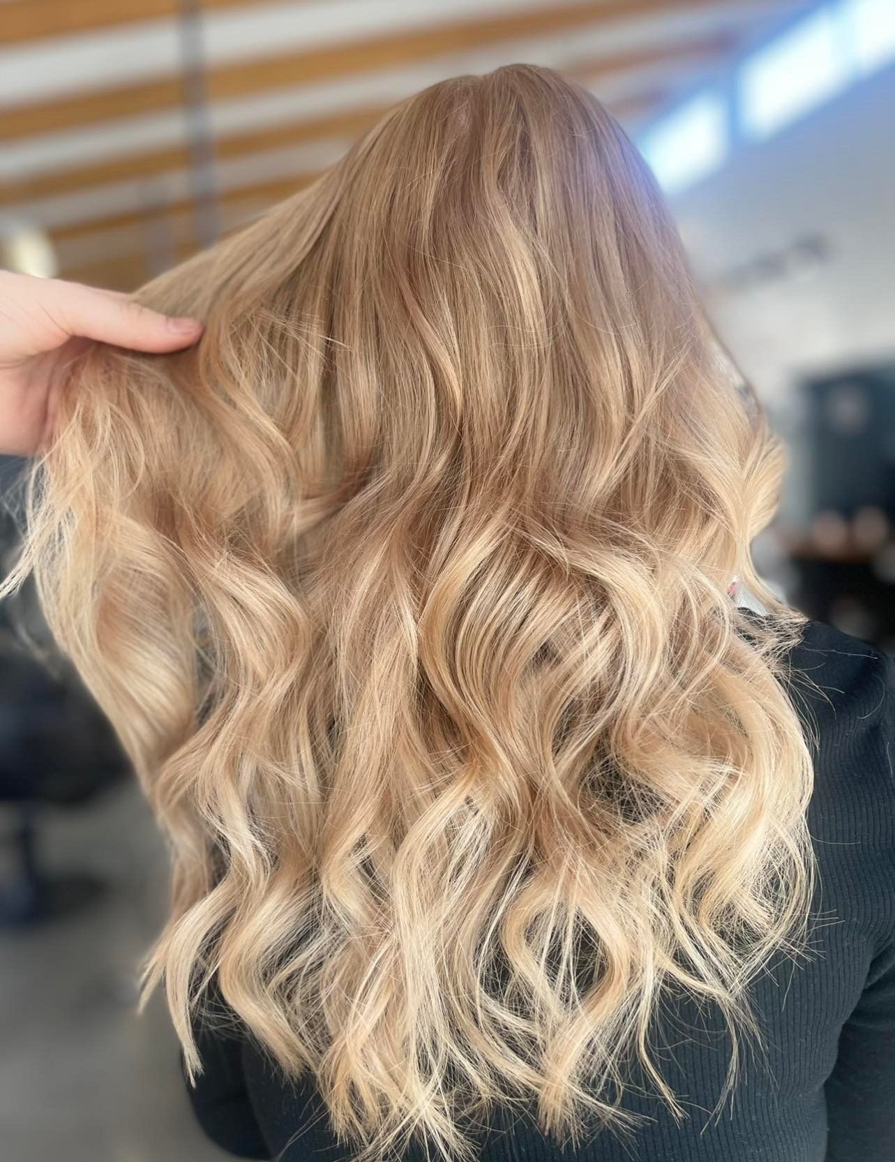 Blonde wavy hair styled, someone's hand in it, indoors, with soft lighting.