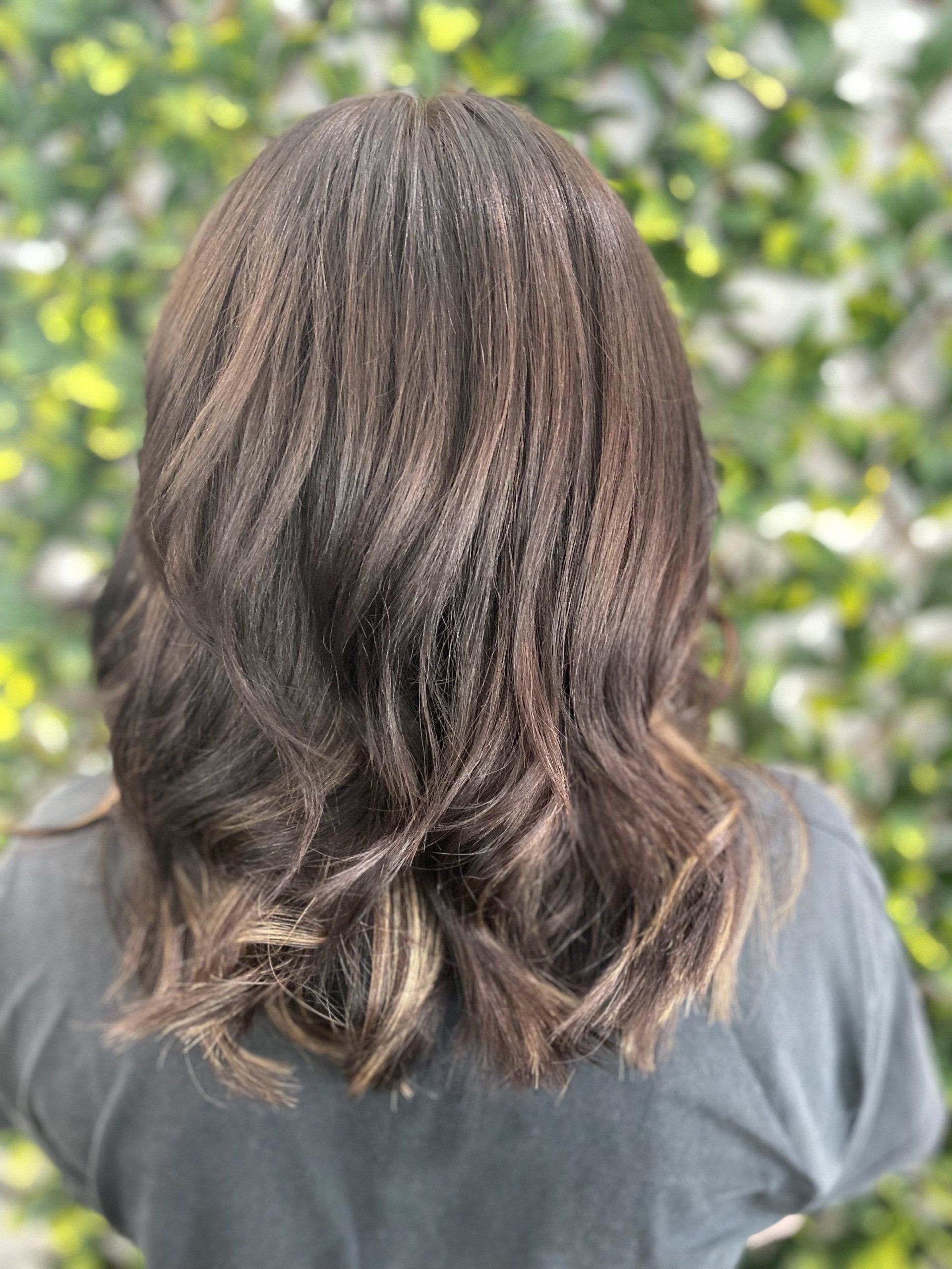 Woman with brown wavy hair, textured from a crimper, against a blurred green backdrop.