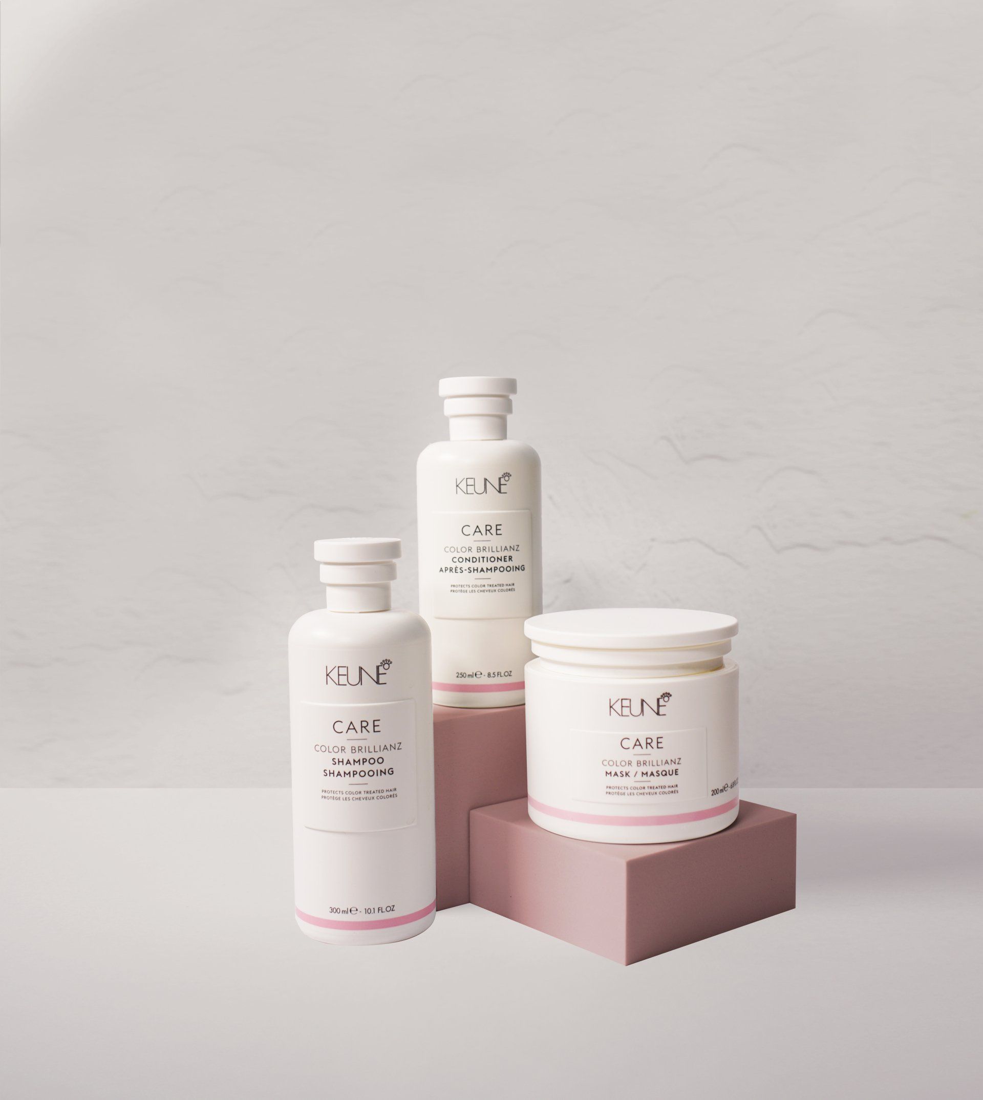 Three white skincare products with pink accents on a pink block against a white background.
