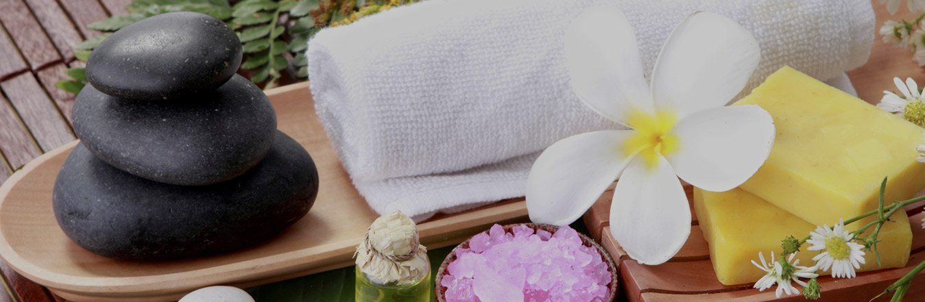 Allestimento da spa con pietre nere impilate, asciugamani bianchi, un fiore e saponi gialli.