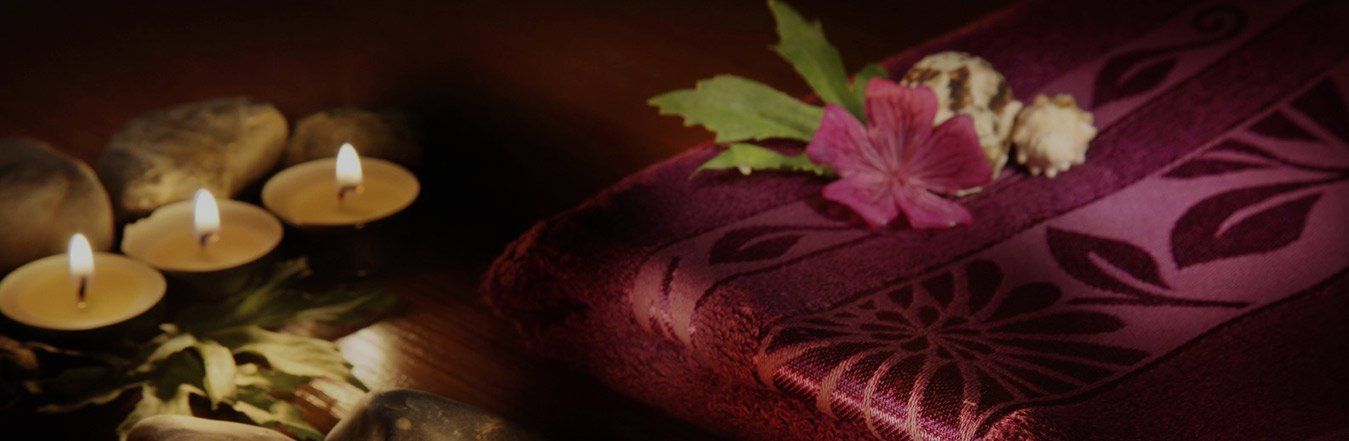 Tre candele, pietre e tessuto viola con fiori, creano un'atmosfera rilassante, simile a quella di una spa.