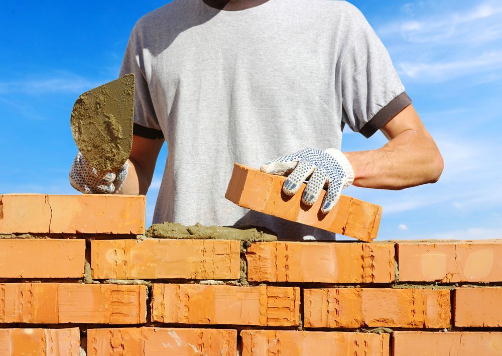 A Man Is Laying Bricks On A Brick Wall — Heritage Bricklaying & Remedial Services In Toukley, NSW