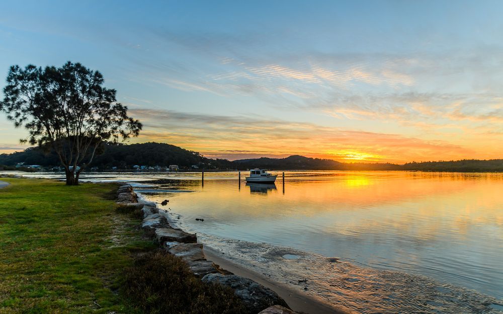 A Sunset Over A Body Of Water With A Boat In The Water — Heritage Bricklaying & Remedial Services In Woy Woy, NSW