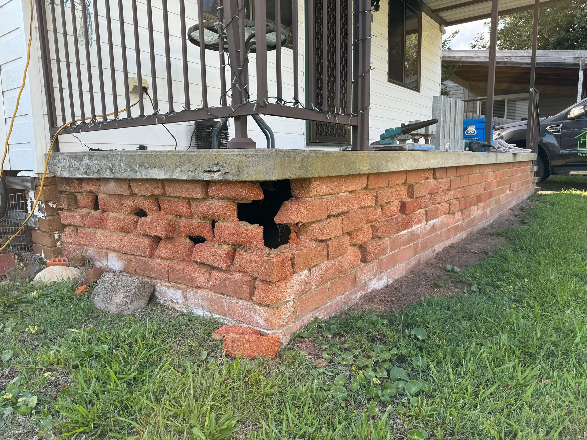 A Brick Wall With Holes In It Is Sitting In The Grass — Heritage Bricklaying & Remedial Services In Jilliby, NSW