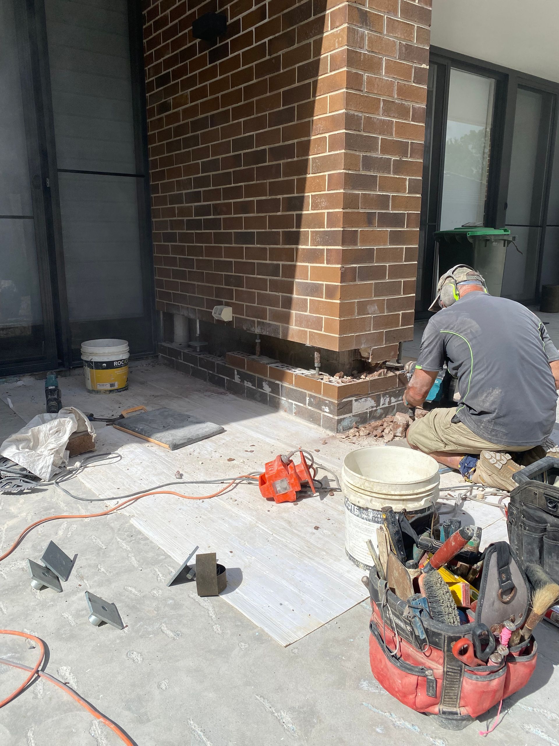 A Man Is Sitting On A Ladder Working On A Brick Wall — Heritage Bricklaying & Remedial Services In Jilliby, NSW