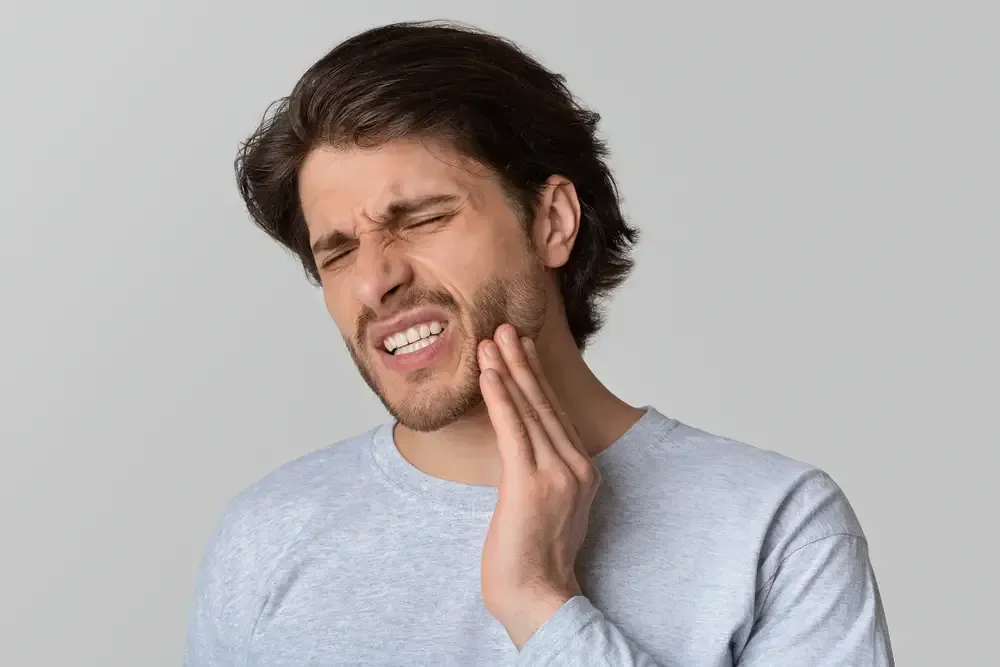 Man in pain, clutching jaw, eyes squeezed shut, likely experiencing toothache.