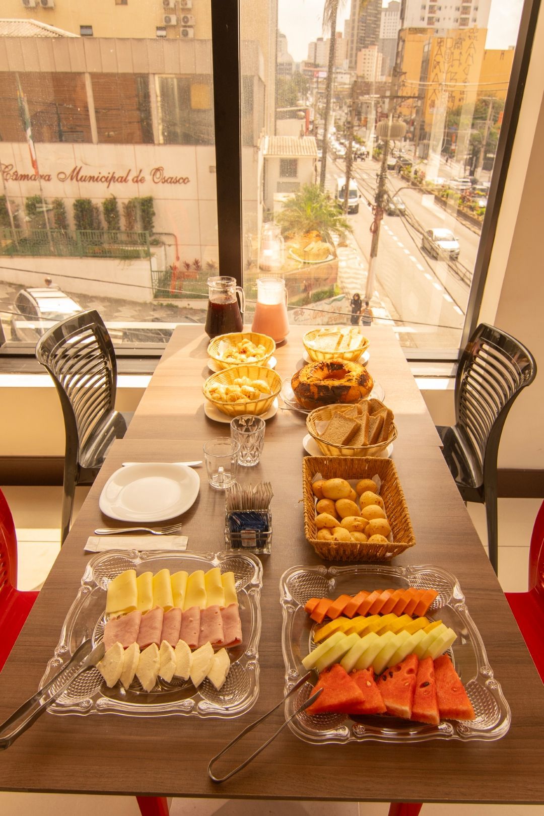 Uma mesa com pratos de comida e frutas em frente a uma janela.