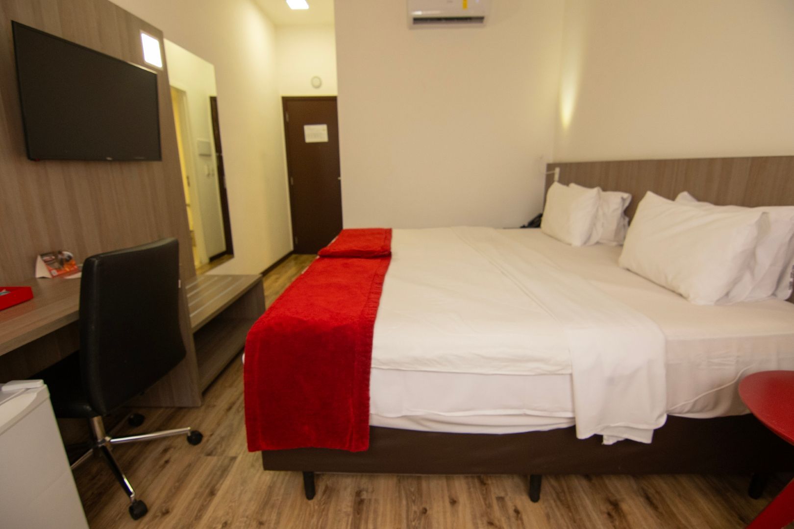 Um quarto de hotel com uma cama, escrivaninha, cadeira e televisão.