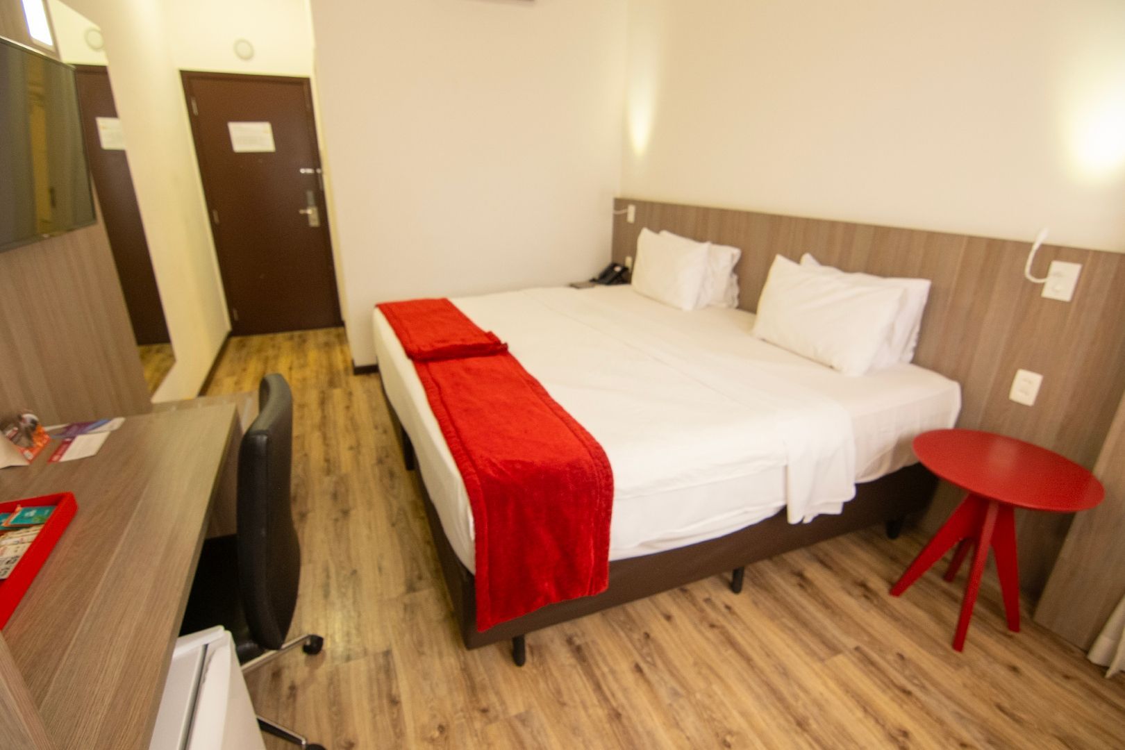 Um quarto de hotel com duas camas, uma escrivaninha e uma mesa vermelha.