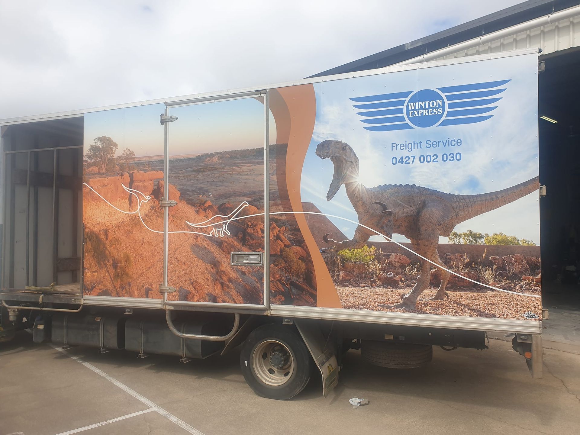 A truck with a picture of a dinosaur on the side is parked in a parking lot.