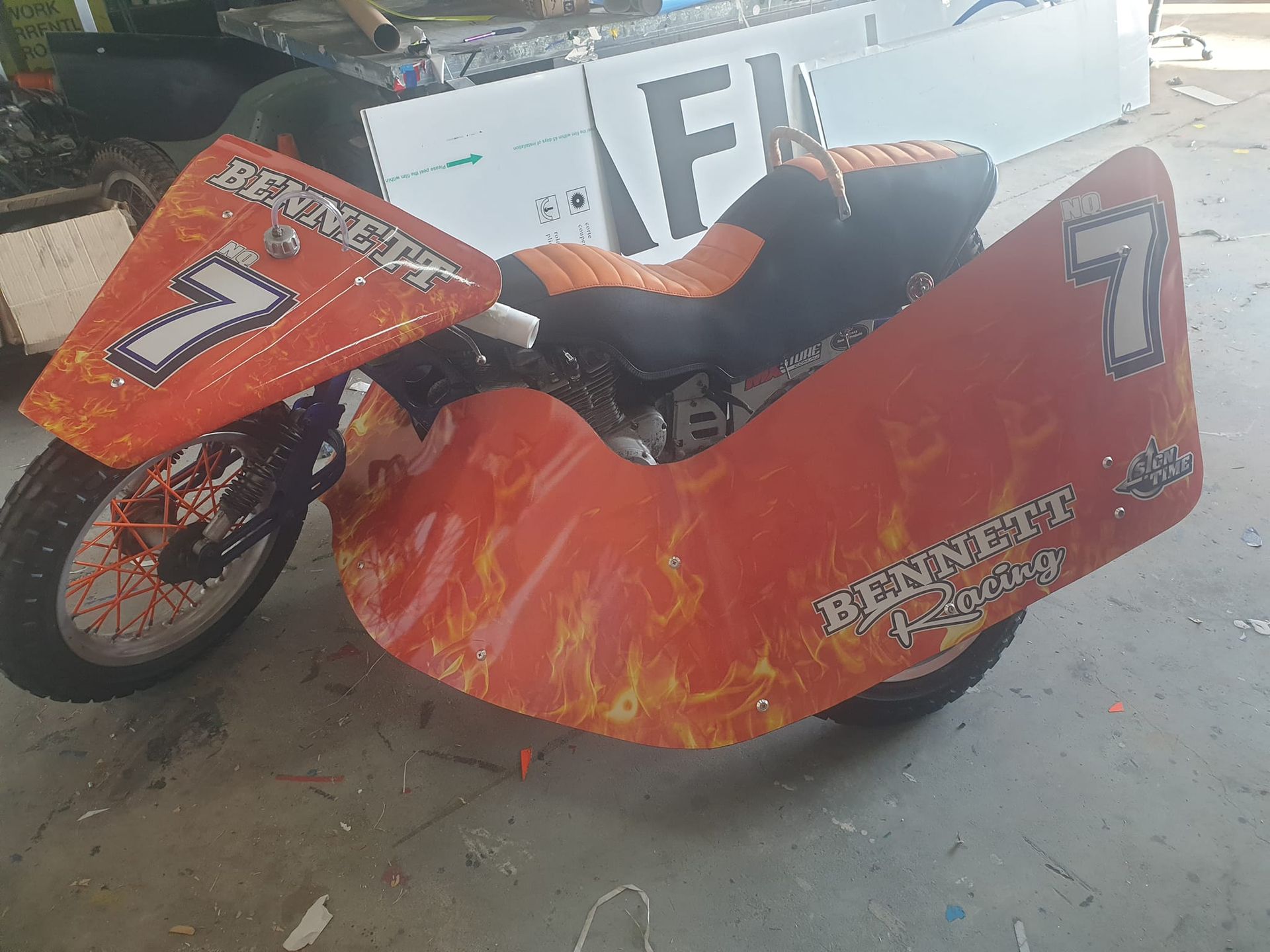 An orange motorcycle with the number 7 on the side is parked in a garage.