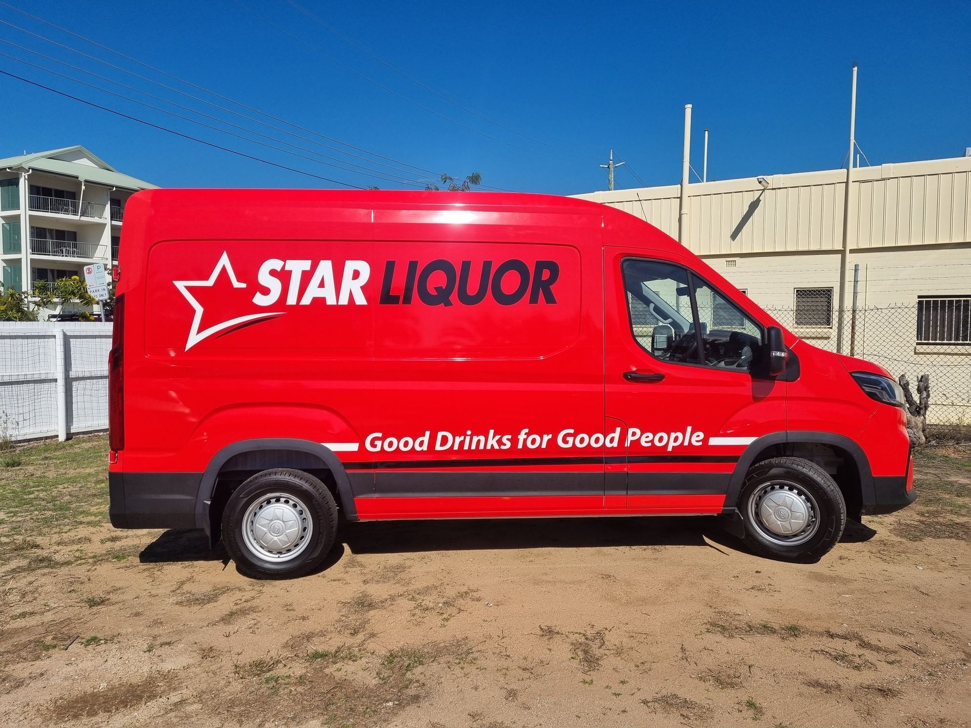 A red van with the word liquor on it is parked in a dirt field.