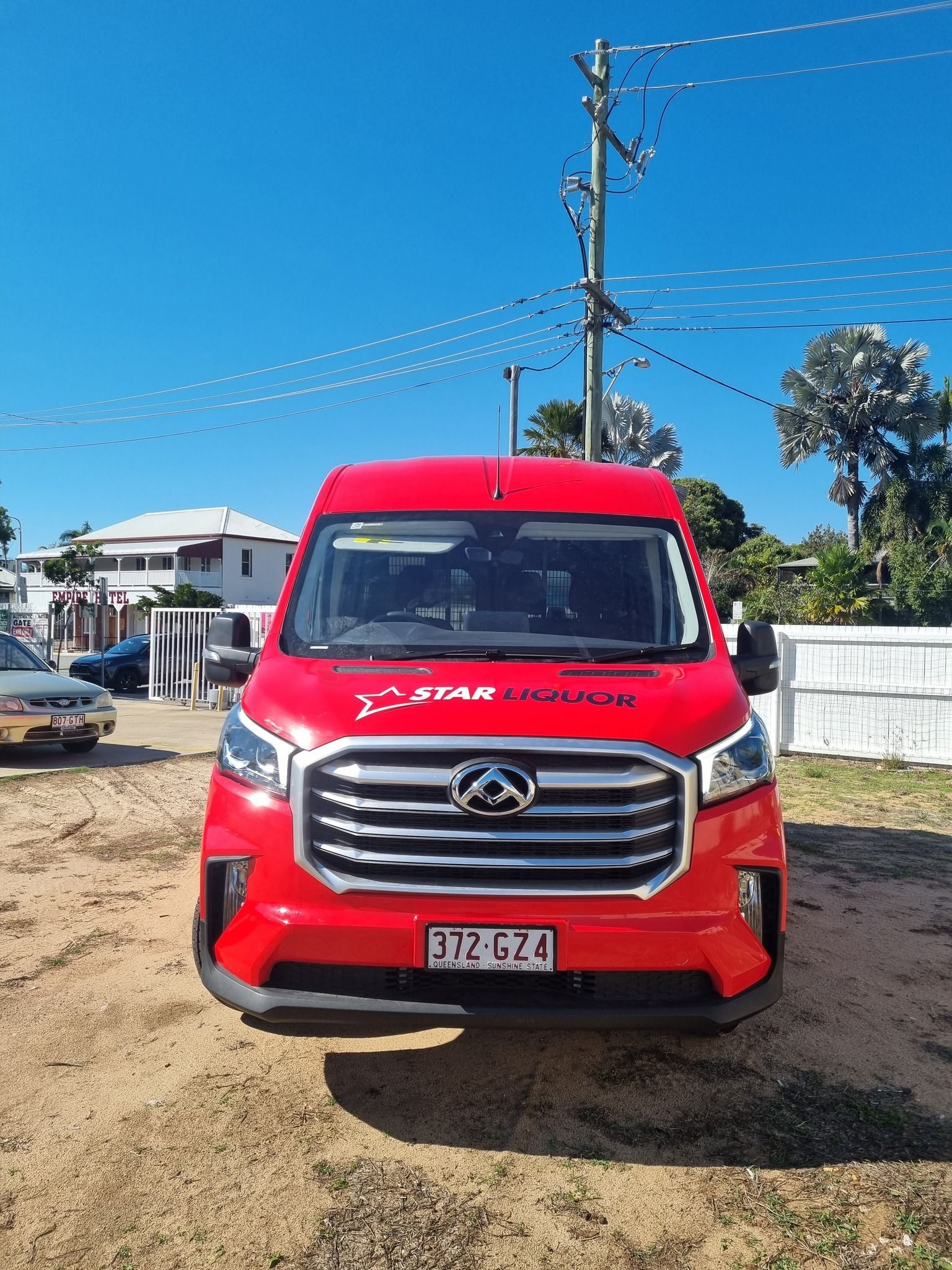 A red van is parked in a dirt lot next to a power pole.