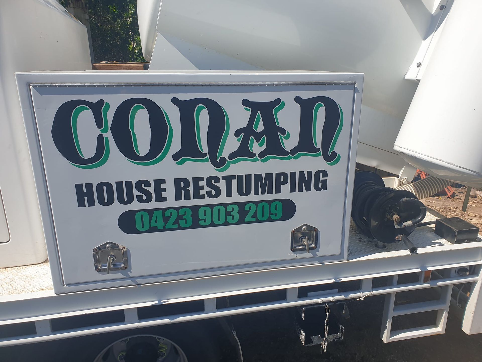 A white truck with a sign on the back that says conan house restumping